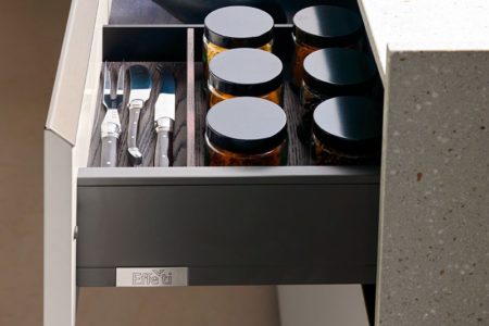 Cassetto aperto della cucina senza maniglie moderna E0, con divisori in legno e spezie conservate in barattoli.
