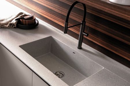 Dettaglio del lavello della cucina con gola E0, con un piano di lavoro chiaro e la parete retrostante in legno scuro.