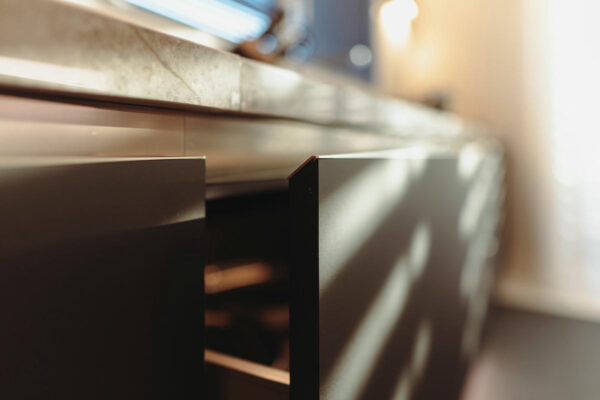 Dettaglio dell'apertura di un cassetto della cucina moderna senza maniglie E0 in versione scura.