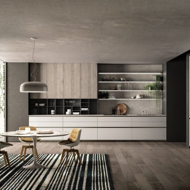 Cucina moderna senza maniglia E0 con pensili bianchi, grigi e color legno e al centro della stanza un tavolo rotondo a tre posti.