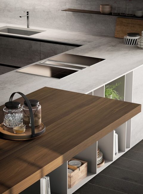 Dettaglio del piano di lavoro della cucina moderna con gola E0, con piano in cemento chiaro, e tavolo integrato in legno.